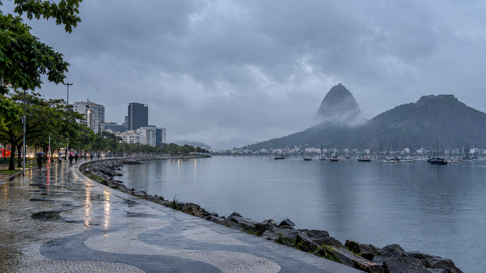 Enseada de Botafogo e Pão de Açúcar sob céu chuvoso, com calçada molhada